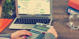 Eine Person arbeitet am Laptop und hält einen Taschenrechner in der Hand. Foto: Pixabay, Firmbee.