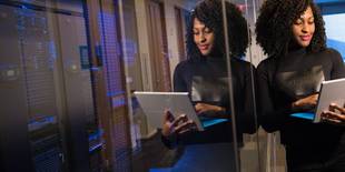 Eine Frau, die mit einem Laptop arbeitet, steht vor einigen Servern; Foto: Unsplash, Christina @ wocintechchat.com