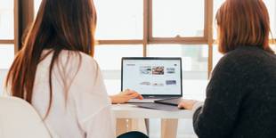 Zwei Frauen, die von hinten zu sehen sind, sind vertieft in einem Gespräch, das Mentoring veranschaulichen soll. Foto: Unsplash, Kobu Agency