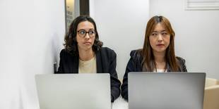 Zwei Frauen an ihren Laptops sehen sich seitlich und abwertend an. Foto: Resume Genius, Unsplash.