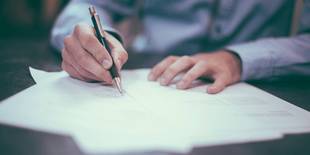 Eine Person, die etwas auf einem Blatt Papier schreibt, ist zu sehen. Foto: Scott Graham, Unsplash.